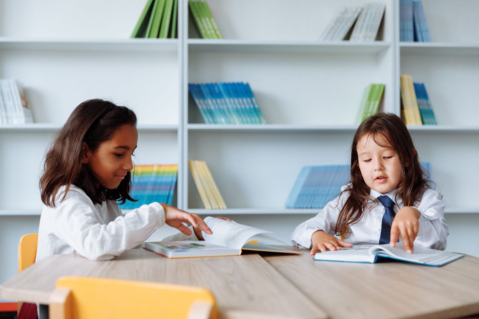 Two young students reading books in a school library lined with bookshelves.