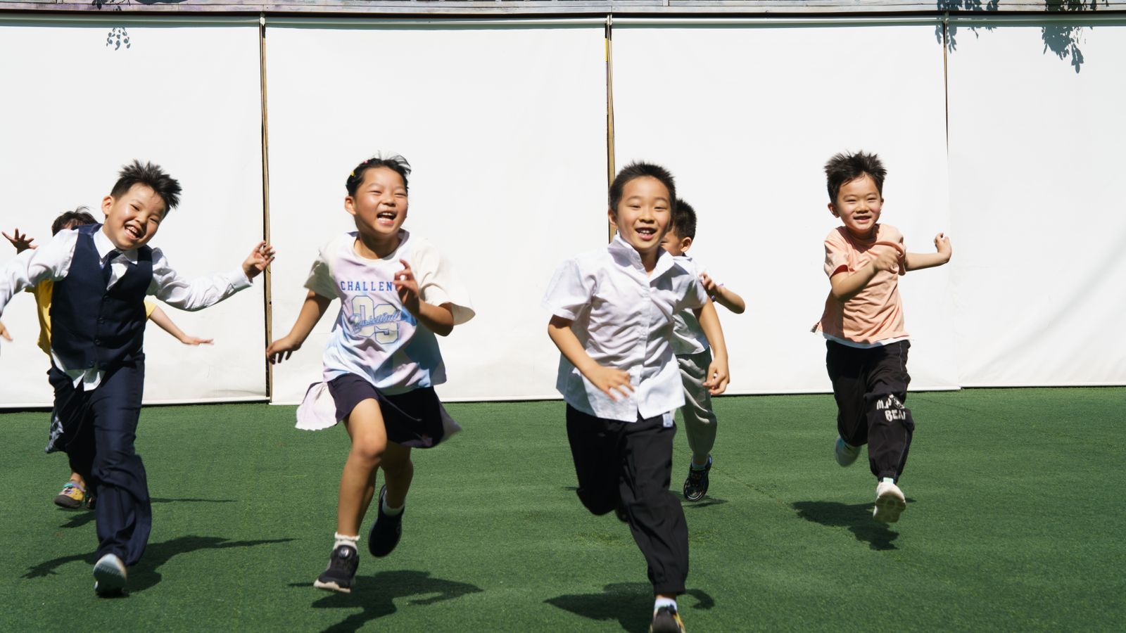 Happy children running outdoors on a green sports ground under bright sunlight.