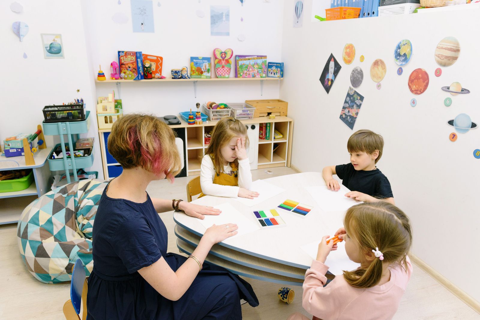 Children doing colourful artwork and craft activities with a teacher in a bright classroom.