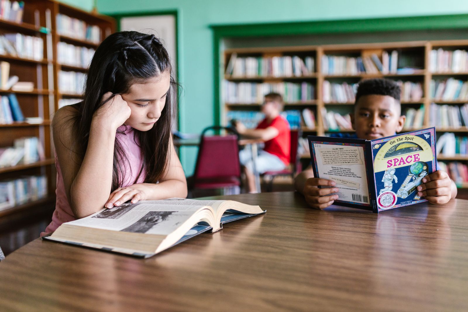 Children reading together at a table in the school library surrounded by books.