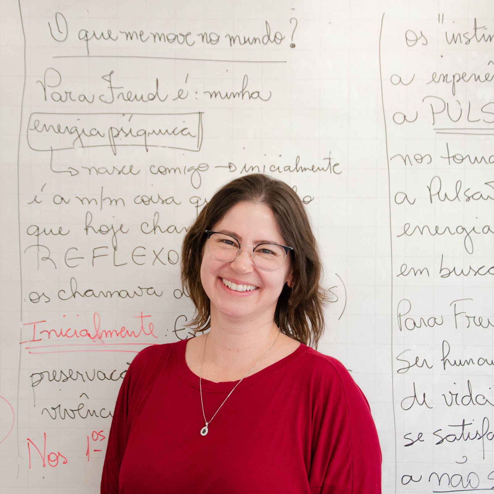 Portrait of a smiling female teacher standing in front of a classroom whiteboard.